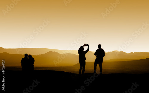 Silhouette of two tourists taking photos of each other at a mountain scene during golden sunset