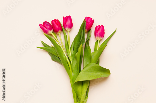 delicate bouquet of red tulips with green leaves on a pastel pink background top view. Easter minimalism concept.