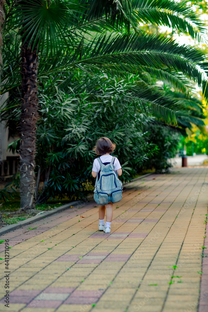 a little girl, a schoolgirl, goes to school on the street with a denim backpack, and in a medical mask a little girl, a schoolgirl, goes to school on the street with a denim backpack, and in a medical mask