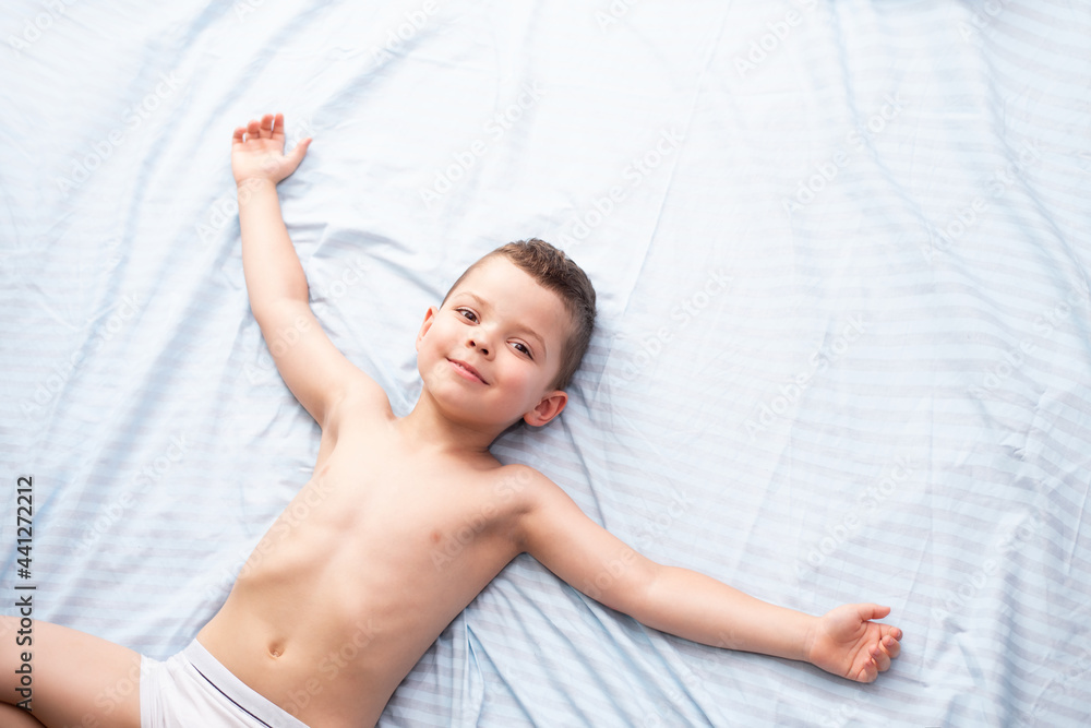 A little five-year-old boy in white underwear lies relaxed on a light blue  bed and smiles. Stock Photo | Adobe Stock