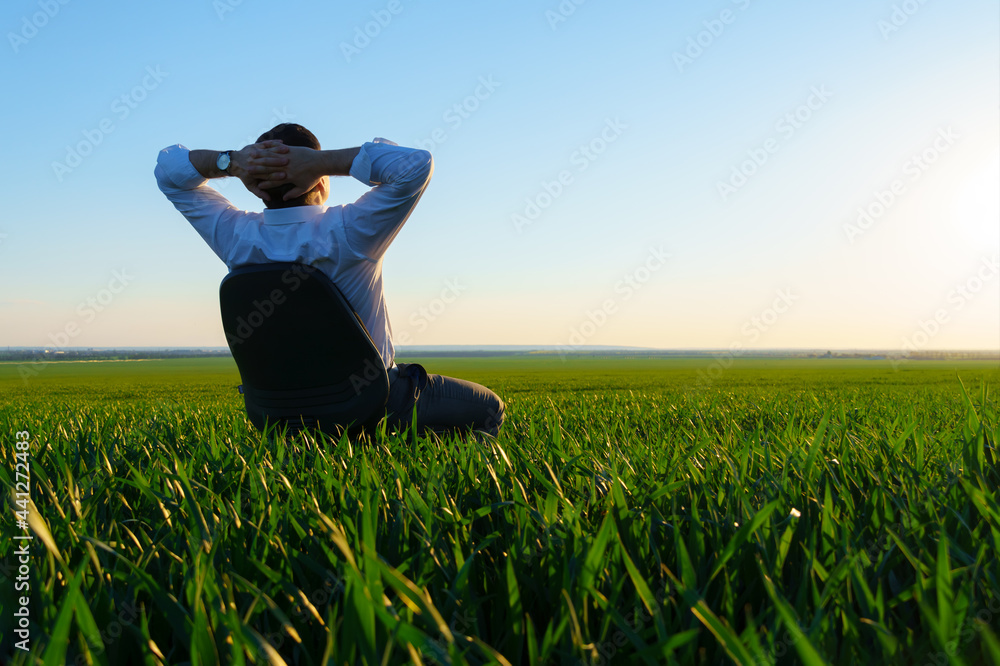 businessman sits in an office chair in a field and rests, freelance and business concept, green grass and blue sky as background businessman sits in an office chair in a field and rests, freelance and business concept, green grass and blue sky as background
