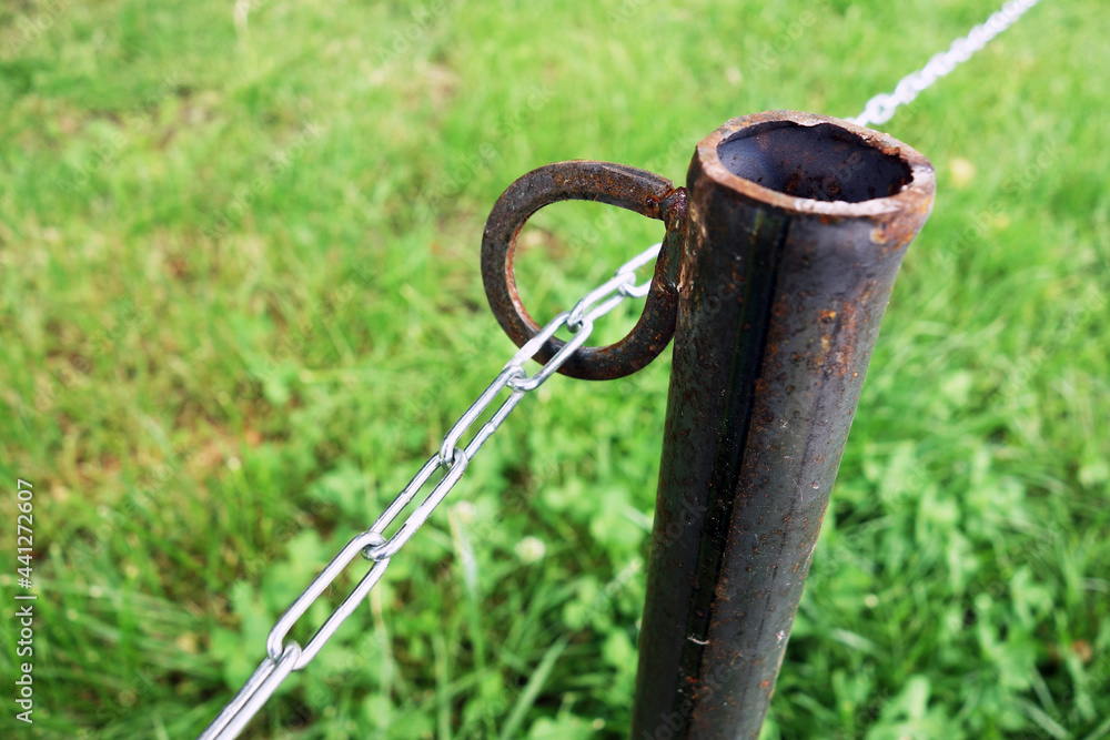 A steel chain leads through an iron loop on a pole in the park A steel chain leads through an iron loop on a pole in the park