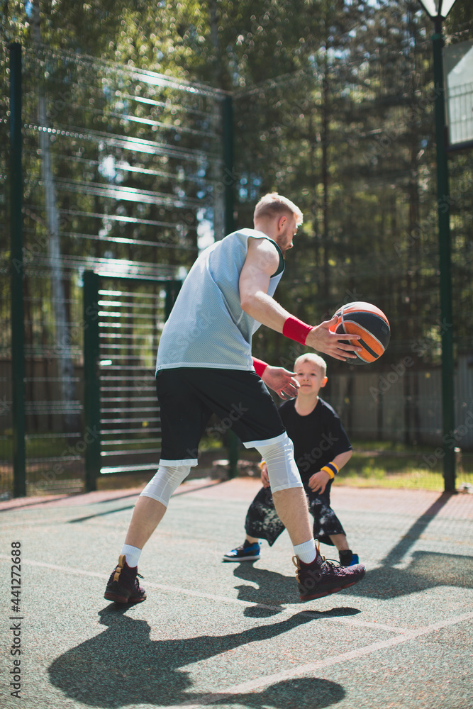 American athletes trainer and little boy kid playing basketball outdoors. Basketball athlete training on court