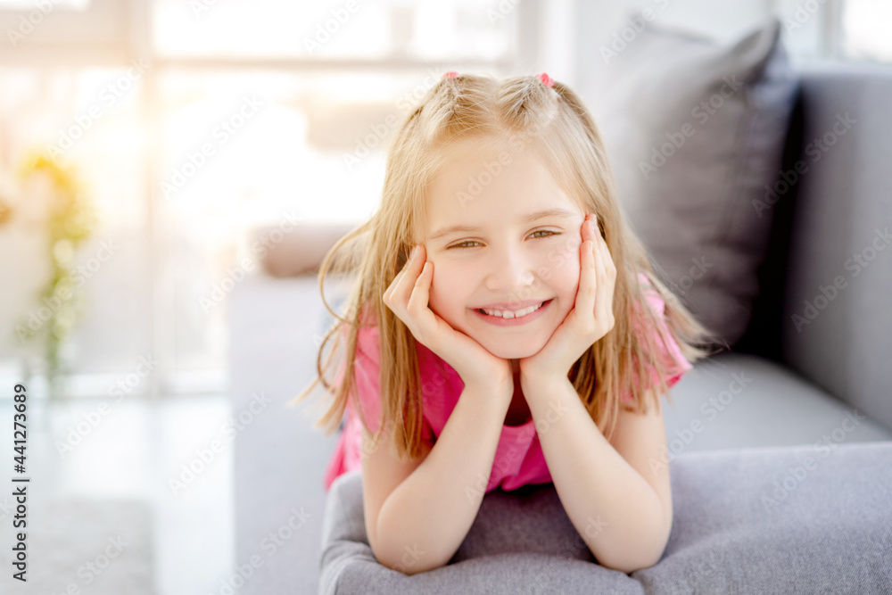 Happy little girl resting on sofa with head on hands indoors Happy little girl resting on sofa with head on hands indoors