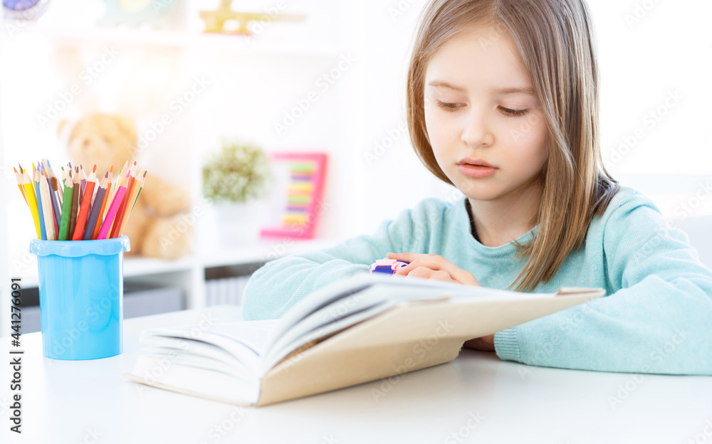 Cute little girl reading book on desk in bright room Cute little girl reading book on desk in bright room