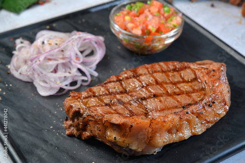 grilled beef steak with suce and fresh onion on dark square plate