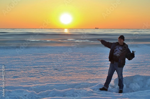 A man standing on the shore of the icy winter coast of the sea against the backdrop of the sunset