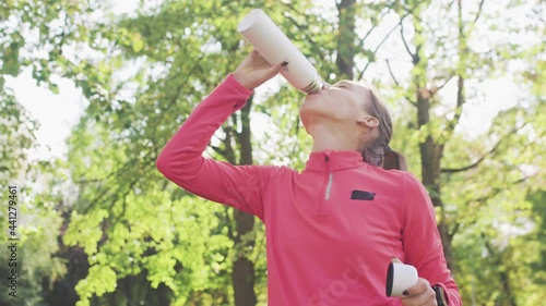 Fitness girl in pink sportswear drinking water from a bidon in the park photo