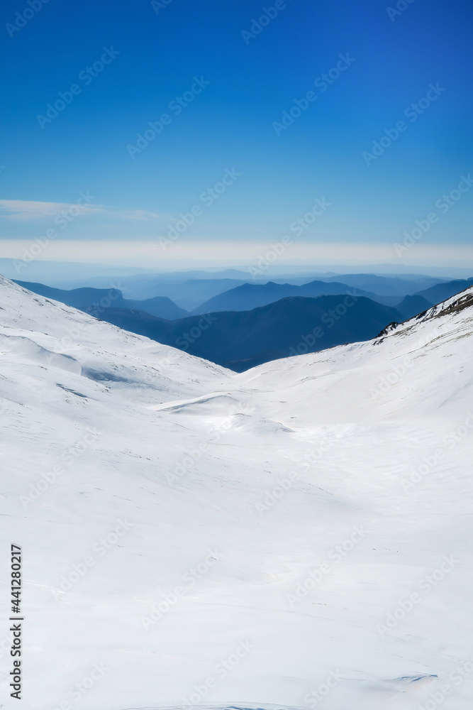 snowy landscape on the top of a mountain, in the background other mountains melting against the horizon with a clear sky, vertical
