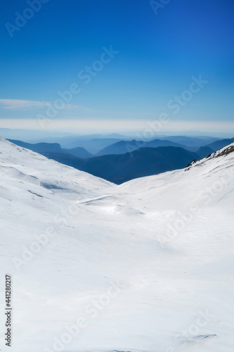 snowy landscape on the top of a mountain, in the background other mountains melting against the horizon with a clear sky, vertical © Javier