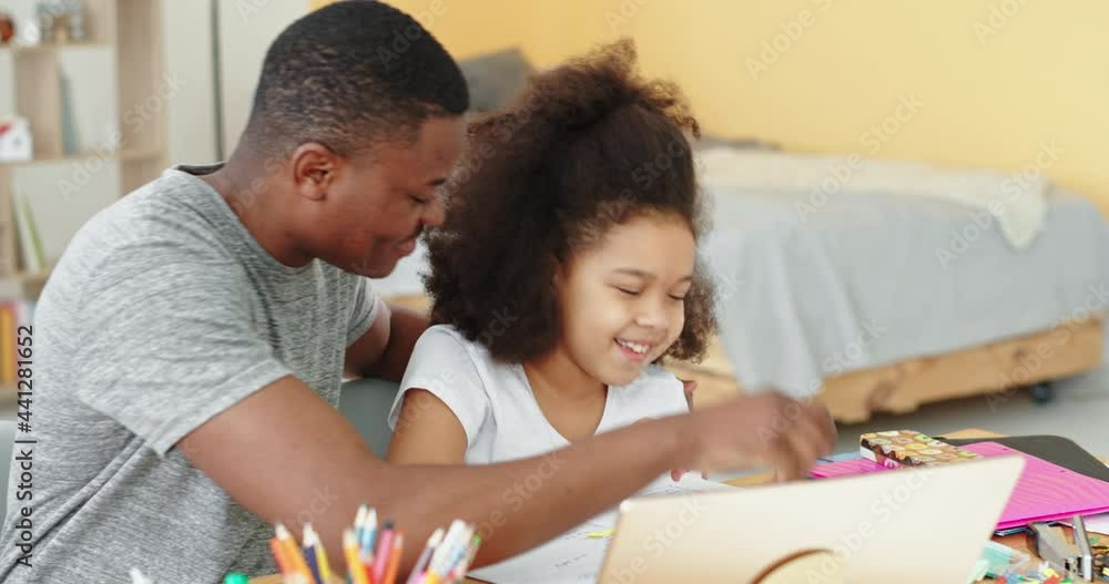 Learning online fun smiling positive emotions give five black family afro american dad teaches lessons at home with his daughter sitting at the table and laptop Learning online fun smiling positive emotions give five black family afro american dad teaches lessons at home with his daughter sitting at the table and laptop