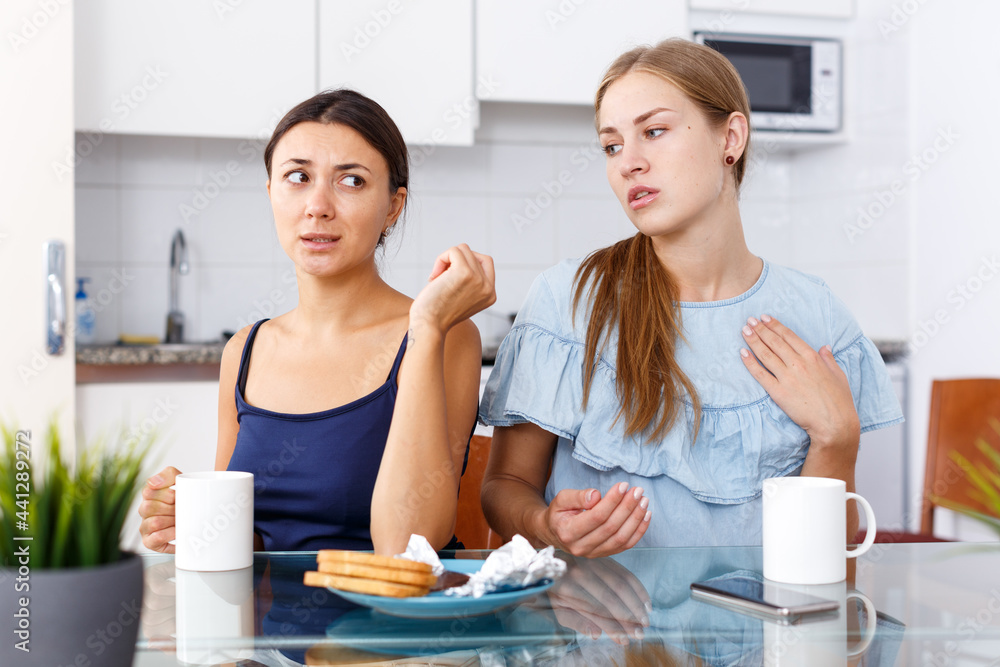 Young woman and her sad friend finding out relationship after quarrel at kitchen