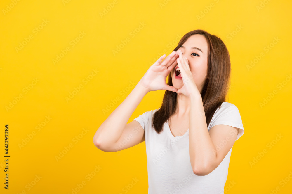 Asian happy portrait beautiful cute young woman teen standing big shout out with hands next mouth giving excited positive looking to side isolated, studio shot on yellow background with copy space Asian happy portrait beautiful cute young woman teen standing big shout out with hands next mouth giving excited positive looking to side isolated, studio shot on yellow background with copy space