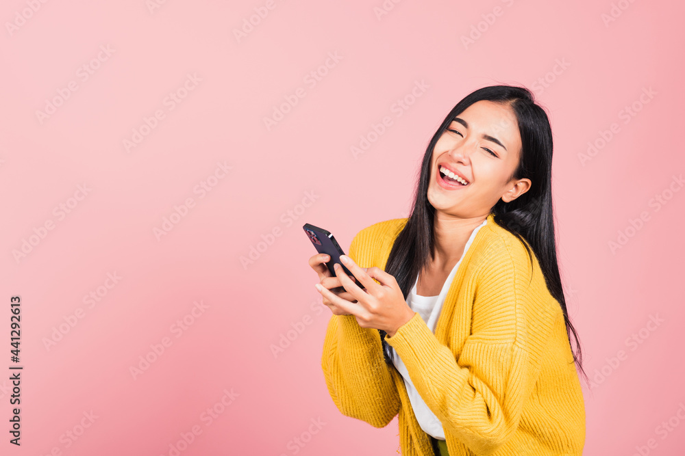 Happy Asian portrait beautiful cute young woman excited laughing holding mobile phone, studio shot isolated on pink background, female using funny smartphone making winner gesture Happy Asian portrait beautiful cute young woman excited laughing holding mobile phone, studio shot isolated on pink background, female using funny smartphone making winner gesture