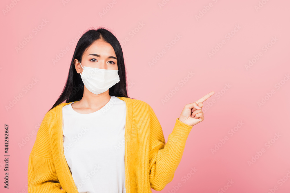 Asian beautiful young woman wearing medical mask protection prevent infection coronavirus, COVID-19 she's pointing finger to space, studio shot isolated on pink background, medical health care concept Asian beautiful young woman wearing medical mask protection prevent infection coronavirus, COVID-19 she's pointing finger to space, studio shot isolated on pink background, medical health care concept