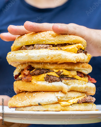 Hand holding a stack of juicy bacon cheeseburgers