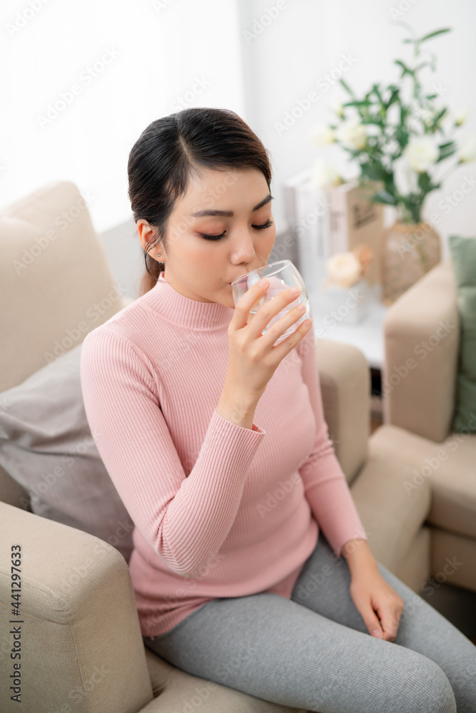 Happy woman taking a vitamin pill sitting on a couch in the living room at home Happy woman taking a vitamin pill sitting on a couch in the living room at home