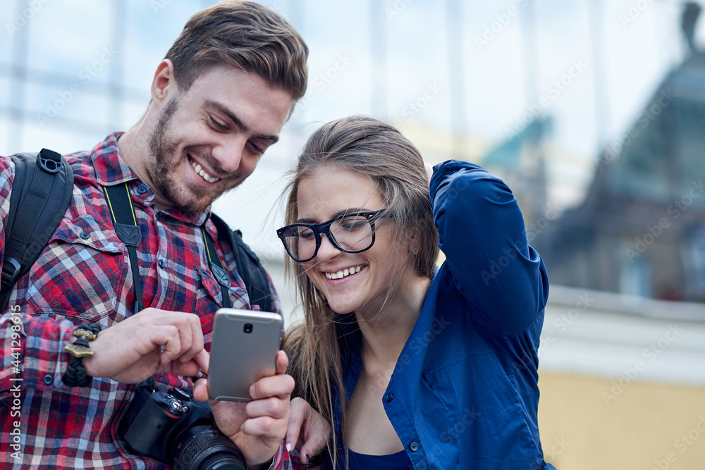 Fototapeta premium Happy couple with smart phone. Happy young loving couple standing outdoors together and looking at the mobile phone together