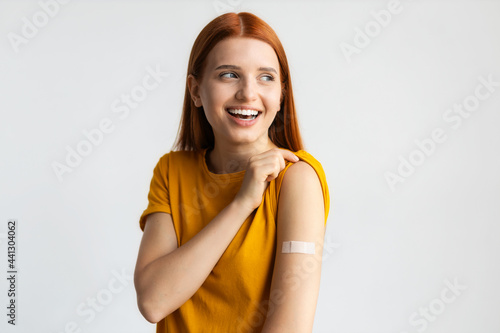 Foto Covid-19 vaccinated caucasian smiling young woman showing arm with plaster, gray