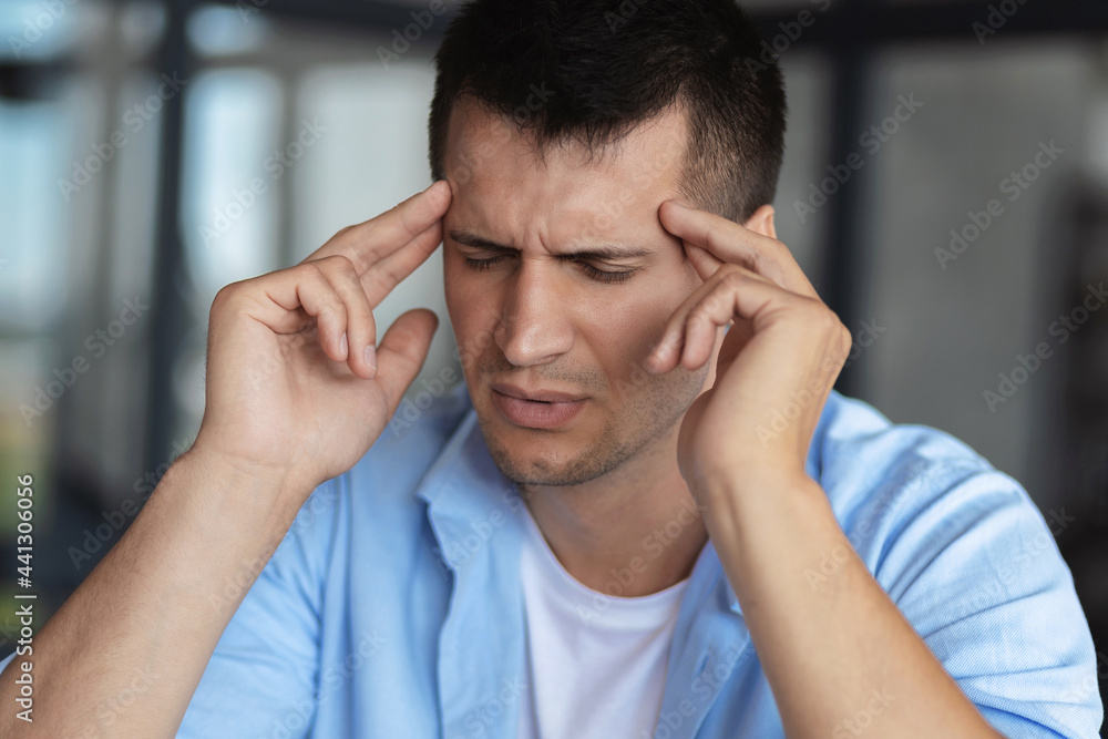 Portrait of young caucasian man, massaging touching temples having severe headache or migraine, close up Portrait of young caucasian man, massaging touching temples having severe headache or migraine, close up