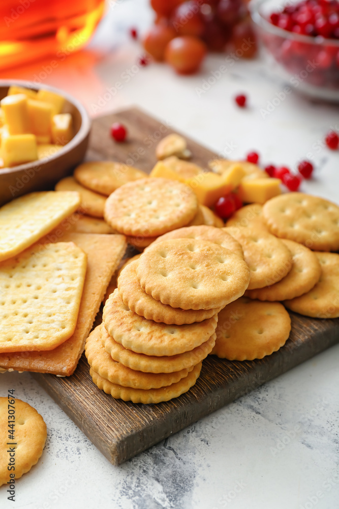 Board with tasty crackers with cheese and snacks on light background Board with tasty crackers with cheese and snacks on light background