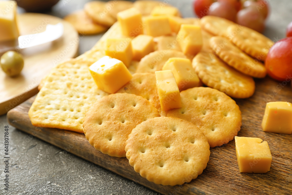 Board with tasty crackers with cheese on grey background Board with tasty crackers with cheese on grey background