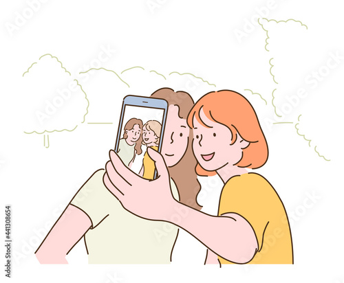 Two friends are taking a selfie with their mobile phones. hand drawn style vector design illustrations. 