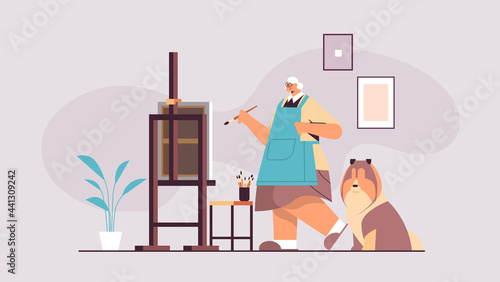 senior woman artist with dog painting picture in workshop creative hobby concept