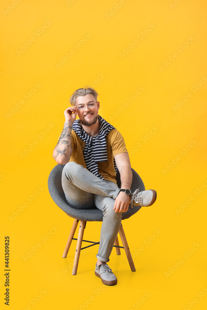 Fototapeta premium Handsome young man sitting in armchair on color background