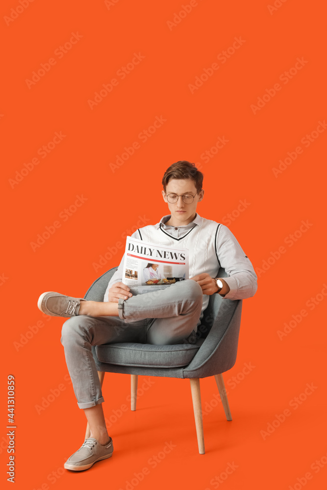 Young man reading newspaper while sitting in armchair on color background Young man reading newspaper while sitting in armchair on color background