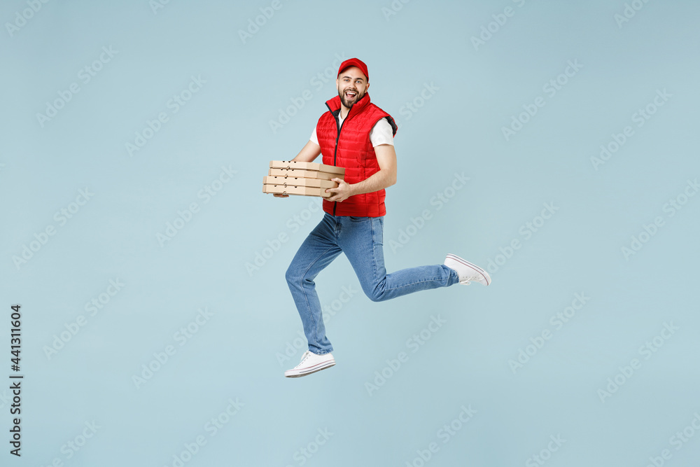Full size body length side view delivery guy employee man in red cap white T-shirt vest uniform work dealer courier jump run go walk isolated on pastel blue color background studio. Service concept