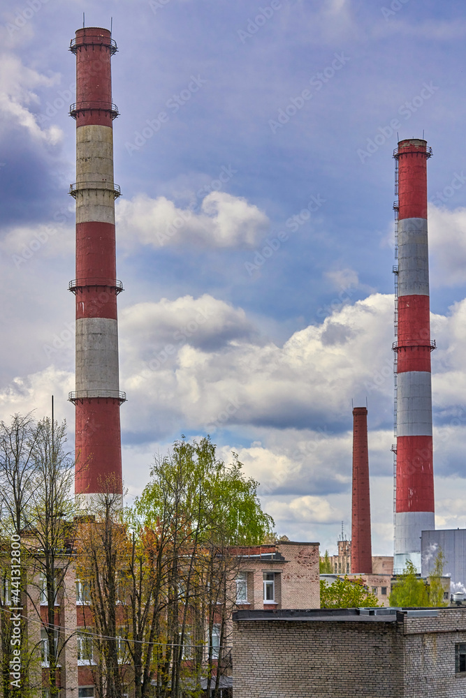 Tall factory chimneys against backdrop of a cloudy sky and residential buildings