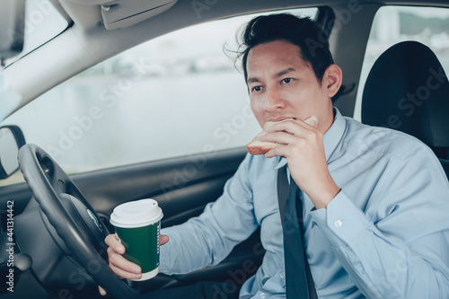 A businessman eating whole wheat toast and holding a coffee cup While driving on the road and he did not lose a seat belt.