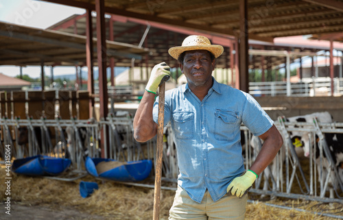 Hired worker with agricultural tool in hands in a cowshed