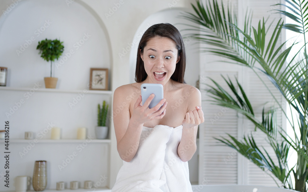 Excited multicultural asian girl holding smart phone screaming yes winning online game, celebrating bid win victory, getting ecommerce shopping offer, during body care and beauty procedure in bathroom Excited multicultural asian girl holding smart phone screaming yes winning online game, celebrating bid win victory, getting ecommerce shopping offer, during body care and beauty procedure in bathroom