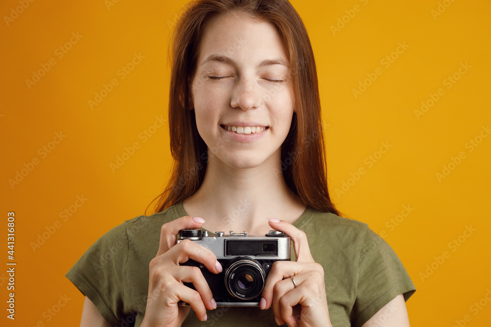 A surprised pretty girl with an open mouth using an old vintage camera on a yellow background. Portrait on an empty background, space for text.