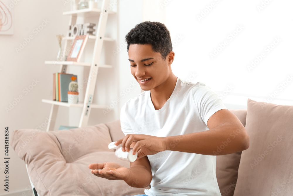 African-American teenage boy taking fish oil pill at home - obrazy, fototapety, plakaty 