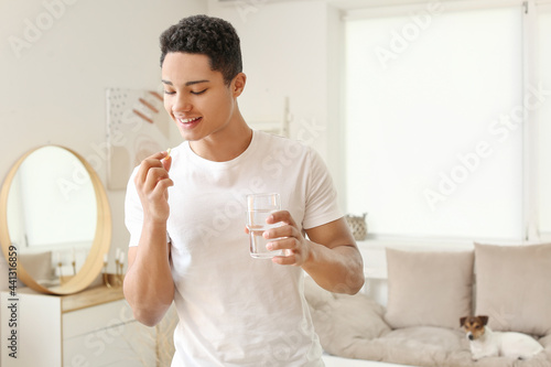 African-American teenage boy taking fish oil pill at home