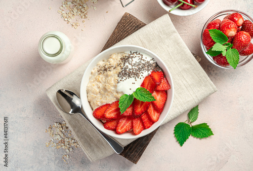 Healthy breakfast with oatmeal with strawberries and chia seeds on a pink background.