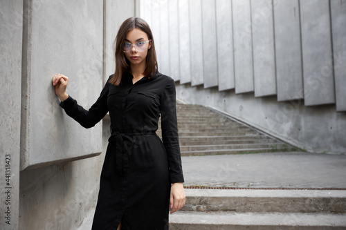 Fashion portrait of a sexy brunette woman with a make up wearing black clothes. She is wearing black modern dress, white sneakers and glasses