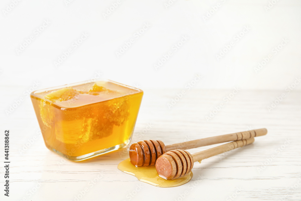 Glass bowl with sweet honey and dippers on light wooden background, closeup Glass bowl with sweet honey and dippers on light wooden background, closeup