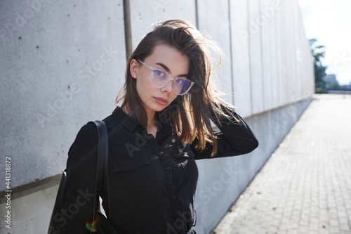 Business woman portrait in city streets at sunset. Sexy brunette wearing black dress, glasses and black leather bag