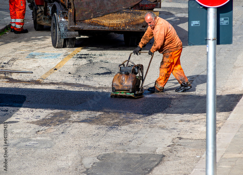 worker leveling fresh asphalt during asphalt pavement repair or construction works