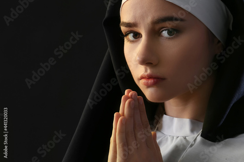Young praying nun on dark b...