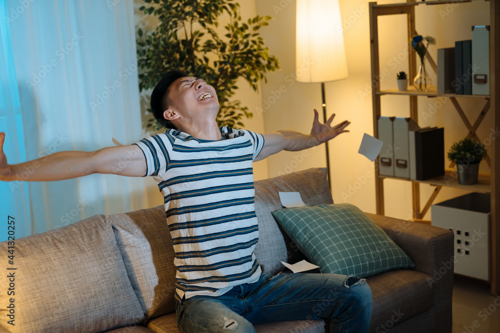 happy successful young Asian billionaire man smiling happily open arms stretching and looking up. Wealth investment economic concept. cheerful male sitting in home living room couch win lottery happy successful young Asian billionaire man smiling happily open arms stretching and looking up. Wealth investment economic concept. cheerful male sitting in home living room couch win lottery
