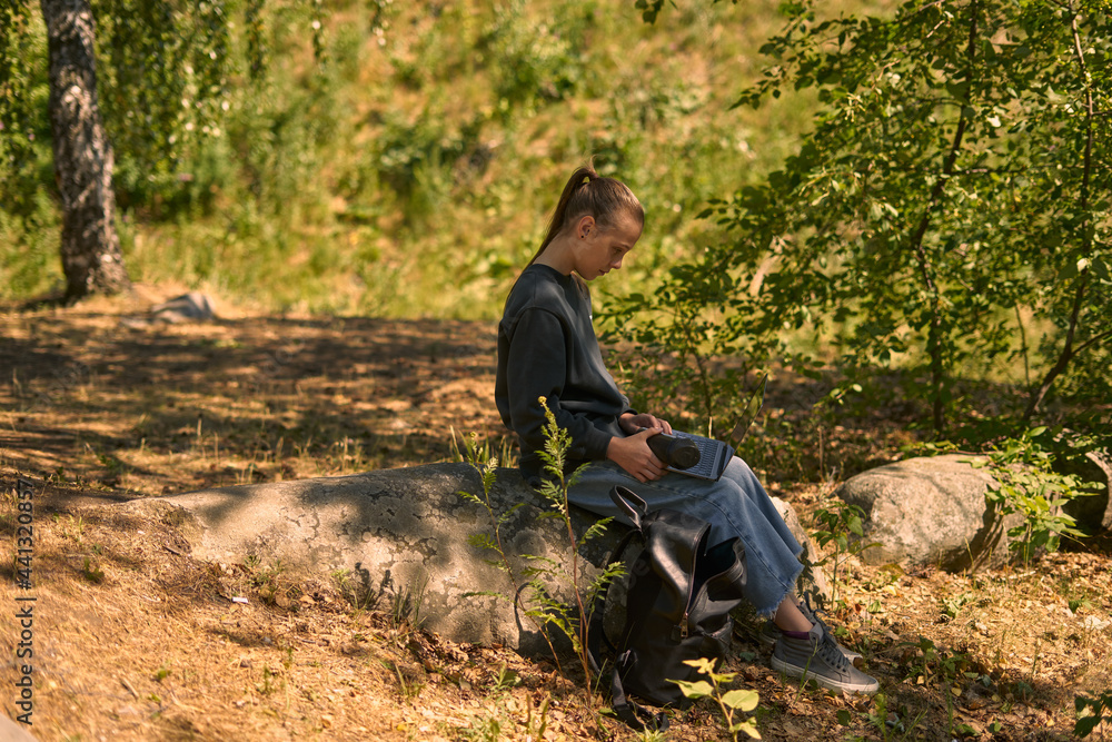 a young girl in nature in the forest sits on a rock and communicates online on the Internet via a laptop a young girl in nature in the forest sits on a rock and communicates online on the Internet via a laptop
