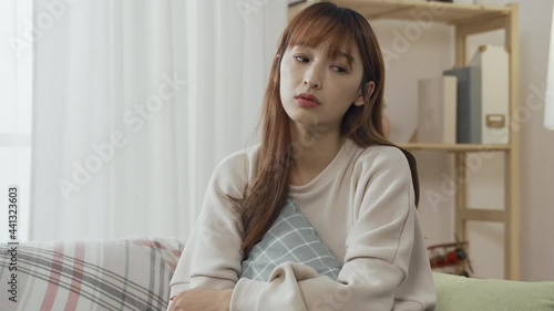 korean woman holding pillow in arms is thinking dully about her weekend plan in living room. boring asian young female sitting alone lets out a soft sigh feeling like doing nothing at home. photo