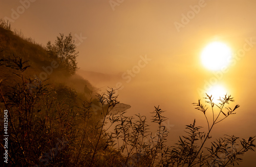 Everything is flooded with the yellow light of the rising sun, the silhouette of a fisherman on the river bank. Oka River, Ryazan region, Russia.