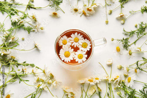 Composition with cup of chamomile tea and flowers on light background