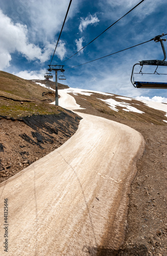 A winding river of dusty brown snow and a cable car on the slopes of Dombay. Caucasus, Russia.